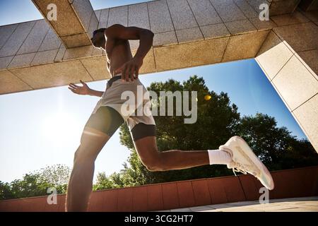 Ein junger Athlet wird während des Laufens im Freien an einem sonnigen Tag in der Mitte der Bewegung festgehalten. Das Bild zeigt dynamische Action, Energie und Fitness in einer urbanen Umgebung Stockfoto