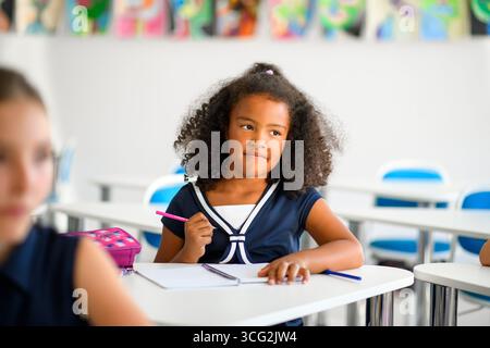Fokussiertes Schulmädchen schreibt Notizen im Klassenzimmer. Stockfoto