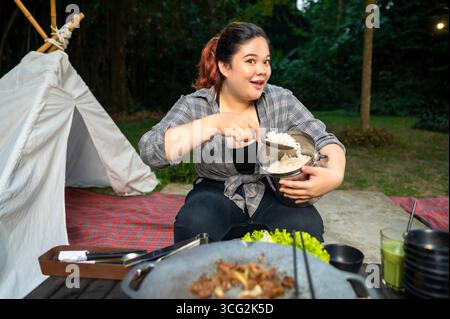 Eine übergewichtige indonesische südostasiatische Frau, die beim Camping einen Metallbehälter mit gekochtem Reis hält. Die Szene des Lebensstils des Genießens von Fo Stockfoto