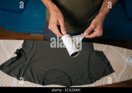 Nahaufnahme des Mannes von oben, der die benutzte Schicht der klebrigen Fusselrolle abzieht, um die Kleidung von Staub, Haaren und Fasern zu reinigen und sicherzustellen, dass die Kleidung verbleibt Stockfoto