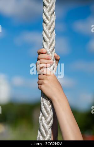 Nahaufnahme von Kinderhänden, die im Freien Sportseil mit klarem Himmel greifen, Konzept von Kraft, Spiel und Aktivität Stockfoto