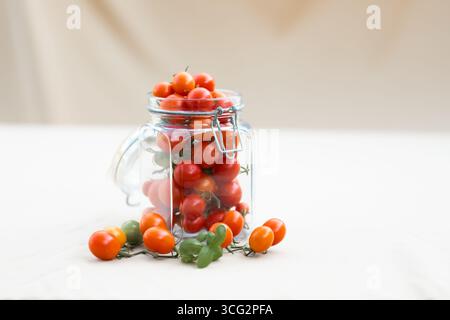 Kirschtomaten in einem Glas mit Basilikumblättern. Konservierung von Lebensmitteln im Herbst oder Winter. Hausgemachte Zubereitungen. Stockfoto