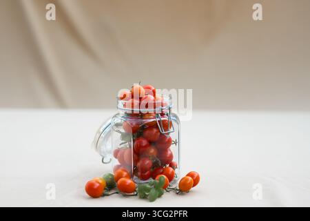 Kirschtomaten in einem Glas mit Basilikumblättern. Konservierung von Lebensmitteln im Herbst oder Winter. Hausgemachte Zubereitungen. Stockfoto