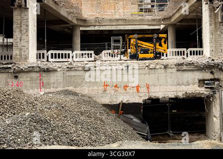 Schwere Maschinen befinden sich auf einer Baustelle, umgeben von Schutt und Schutt. Die Mitarbeiter sind mit Renovierungsarbeiten an der Gebäudestruktur beschäftigt. Zum Schutz sind Sicherheitsbarrieren vorhanden. Stockfoto