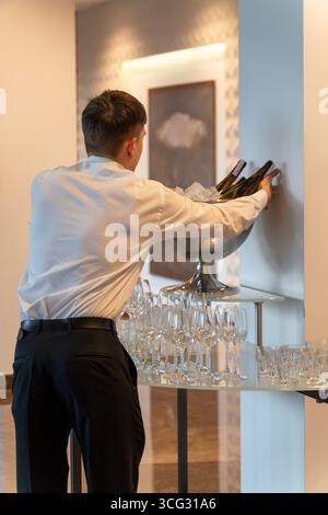Ein Kellner serviert gekühlten Wein und Champagner in einer Metallschale Eis bei einer gehobenen Veranstaltung oder Party in einem modernen Bankettsaal. Stockfoto