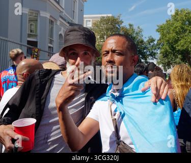 Zwei Freunde posieren für ein Foto, einer trägt einen Hut mit der Hand auf der Schulter, während des Notting Hill Carnival in London. England, 25. August 2025 Stockfoto
