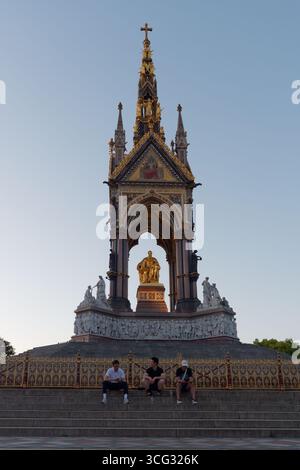Drei Personen sitzen an einem Sommerabend in London auf den Stufen des Albert Memorial. August 2025 Stockfoto