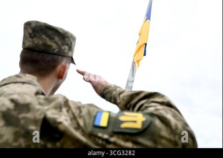 Nicht exklusiv: Ein Soldat in Tarnuniform grüßt vor der ukrainischen Flagge, die während der Flaggenhetzzeremonie am Hetm auf dem Fahnenmast fliegt Stockfoto
