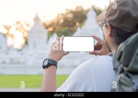 Rückansicht eines jungen Mannes mit Rucksack, der auf Reisen ein Mobiltelefon mit isoliertem Bildschirm hält. Kopierbereich. Stockfoto