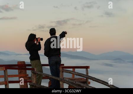 Glückliches junges Paar mit Kamera, das am Aussichtspunkt des Meeres von ​​mist auf einem hohen Berg im Nationalpark steht. Stockfoto