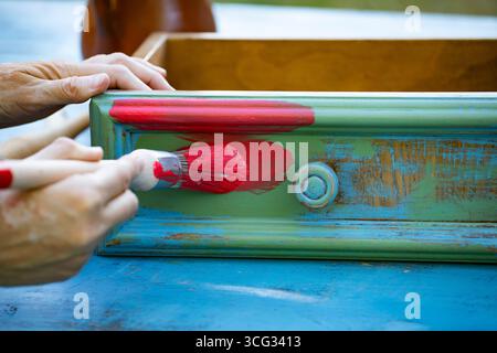 Holzmöbel mit Kreidemalerei aus menschlicher Hand. Alte Holzmöbel werden mit brandneuer, farbenfroher Kreidefarbe erneuert. Die Innendekoration wird neu gestaltet Stockfoto