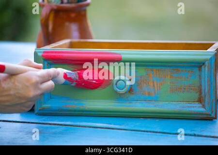 Holzmöbel mit Kreidemalerei aus menschlicher Hand. Alte Holzmöbel werden mit brandneuer, farbenfroher Kreidefarbe erneuert. Die Innendekoration wird neu gestaltet Stockfoto