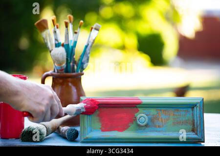 Holzmöbel mit Kreidemalerei aus menschlicher Hand. Alte Holzmöbel werden mit brandneuer, farbenfroher Kreidefarbe erneuert. Die Innendekoration wird neu gestaltet Stockfoto