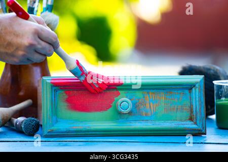 Holzmöbel mit Kreidemalerei aus menschlicher Hand. Alte Holzmöbel werden mit brandneuer, farbenfroher Kreidefarbe erneuert. Die Innendekoration wird neu gestaltet Stockfoto