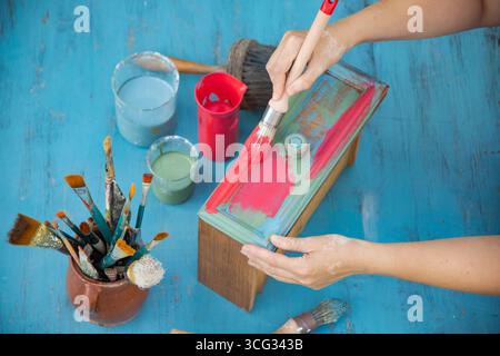 Holzmöbel mit Kreidemalerei aus menschlicher Hand. Alte Holzmöbel werden mit brandneuer, farbenfroher Kreidefarbe erneuert. Die Innendekoration wird neu gestaltet Stockfoto
