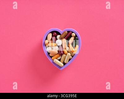 Verschiedene Pillen und Kapseln in einem herzförmigen Behälter, symbolisiert Herz-Kreislauf-Gesundheit und Wohlbefinden Stockfoto