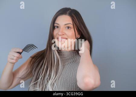 Junge Frau kämmt lange Haarverlängerungen mit einem speziellen Kamm, um Bruch zu verhindern und gesunde Stränge zu erhalten Stockfoto