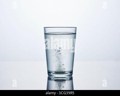 Brausetablette löst sich in einem Glas Wasser auf, produziert eine Kaskade von Blasen und gibt gleichzeitig medizinische Eigenschaften für die Gesundheit frei Stockfoto