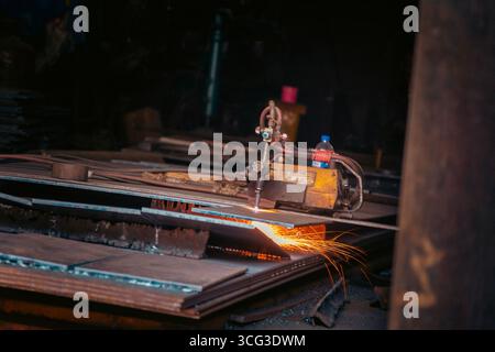 Dieses Bild zeigt einen industriellen Schneidbrenner, der Metallbleche mit hellen Funken und Maschinen in einer Werkstatt durchschneidet Stockfoto
