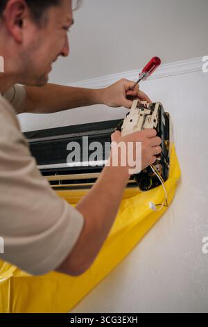 Konzentrierter HLK-Techniker, der die Klimaanlage sorgfältig zerlegt und dabei tropfendes Wasser und Fremdkörper während des Reparaturvorgangs mit einem Schutzbeutel aufgefangen. Stockfoto
