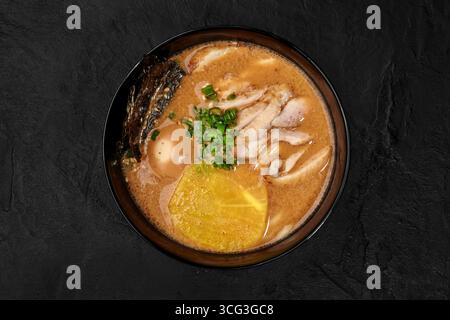 Hühnerramen mit Ei, Nori-Algen, Menma und gehackten grünen Zwiebeln serviert in einer schwarzen Schüssel auf dunklem Hintergrund Stockfoto