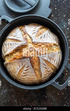 Frisch gebackenes Sauerteigbrot in einem schwarzen gusseisernen Holländischen Ofen. Die rustikale goldene Kruste weist ein künstlerisches Punktmuster auf, das die handgefertigte Farbe hervorhebt Stockfoto