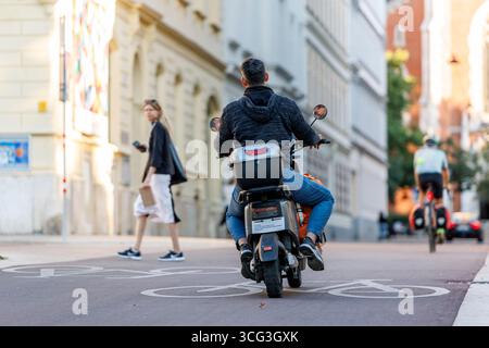 In Wien werden Essenszustellungen durch Lieferdienste wie Foodora, Wolt oder Lieferando durchgeführt. Viele Zusteller befahren mit elektrischen Rollern die Fahrradwege, das für zunehmende Kritik sorgt. Es werden bereits Fahrverbote auf Fahrradwegen für diese Elektromopeds diskutiert. Im Bild: Ein Zustellfahrer mit einem Elektroroller auf einem Fahrradweg am 25. August 2025 auf der Argentinierstraße in Wien. // in Wien erfolgt die Lieferung von Lebensmitteln durch Lieferdienste wie Foodora, Wolt oder Lieferando. Viele Lieferfahrer verwenden elektrische Roller auf Fahrradwegen, was zu einer Zunahme der Fahrten geführt hat Stockfoto