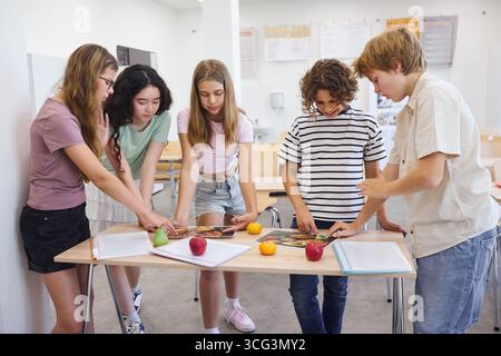Eine Gruppe von Teenagern, die in einem Klassenzimmer zusammenarbeiten und interaktive Bildungsaktivitäten mit frischem Obst und Lernstoff durchführen Stockfoto