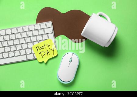 Computertastatur, Haftnotiz und Streich mit verschütteter Tasse Kaffee auf grünem Hintergrund. April-Narrentag-Streich Stockfoto