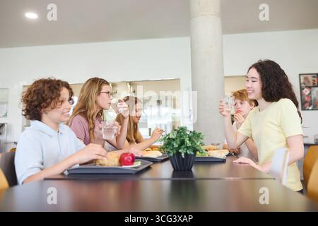 Eine lebhafte Szene von Teenagern, die gemeinsam in einer Schulcafeteria zu Mittag essen, mit freundlichen Interaktionen, verschiedenen Gerichten und einer warmen, sozialen Atmosphäre Stockfoto