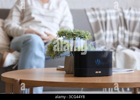 Luftbefeuchter mit Bonsaibaum auf Tisch gegen Frau im Wohnzimmer, Nahaufnahme Stockfoto
