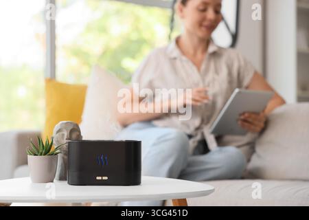 Luftbefeuchter auf dem Tisch gegen Frau mit Tablet-Computer zu Hause, Nahaufnahme Stockfoto