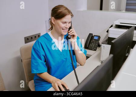 Kaukasische junge Erwachsene Frau nimmt Telefonanruf an, während sie an der Rezeption arbeitet Stockfoto