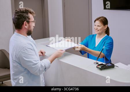 Kaukasische junge Erwachsene Frau überreicht Dokumente an kaukasische Männer mittleren Alters Stockfoto