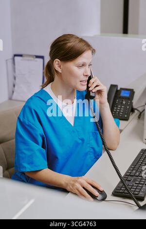 Kaukasische junge Erwachsene Frau, die an der Rezeption arbeitet und Telefonanrufe entgegennimmt Stockfoto