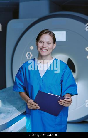 Porträt einer jungen erwachsenen Frau, die lächelt, während sie das Clipboard im MRT-Raum hält Stockfoto