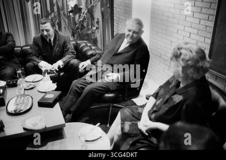 Ludwig Erhard sitzt mit weiteren Personen an einem gedeckten Tisch in einem modernen eingerichteten Raum. Neben ihm seine Ehefrau Luise Erhard. Auf dem Tisch stehen Getränke, Speisen und Zigarrenzubehör. Stockfoto