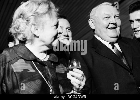 Ludwig Erhard und seine Ehefrau Luise Erhard stehen gemeinsam mit mehreren jüngeren Männern bei einem festlichen Anlass. Beide lachen, Luise Erhard hält ein Glas in der Hand. Stockfoto
