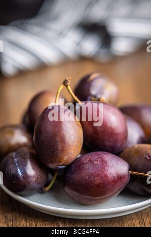 Reife Pflaumen auf einem Teller auf einem Holztisch. Stockfoto