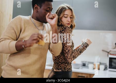 Ein vielseitiges Paar, das einen verspielten Moment genießt, während es in einer modernen Küche tanzt Stockfoto