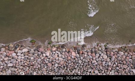 Von oben nach unten auf ein Steinpanzer-Küstenschutzsystem mit Meereswellen, die auf das Ufer treffen, repräsentiert Tiefbau, Klima-ch Stockfoto
