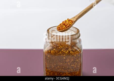Ein Holzlöffel mit Chiliflocken über dem Glasgefäß würzige Würze getrockneter roter Pfeffer Küchenzutat aromatische kulinarische Geschmacksverstärker Lebensmittelzubereitung Stockfoto