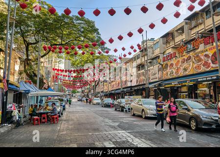 November 2019 - Kuala Lumpur: Berühmte Jalan Alor Food Street in Bukit Bintang, Kuala Lumpur, Malaysia an sonnigen Tagen. Imbissstände im Freien, Cafés, südostasiatische Küche und Gerichte, rote Laternen über dem Kopf, geparkte Autos, Leute gehen oder essen an Tischen Stockfoto