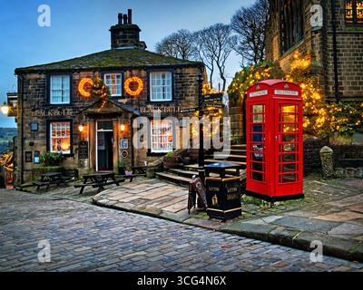 Großbritannien, West Yorkshire, Haworth, Main Street, Black Bull Inn und Red Telephone Box zu Weihnachten. Stockfoto