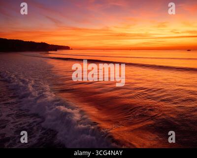 Goldener Sonnenuntergang über den Wellen des Ozeans mit lebendigem Himmel und friedlichem Blick auf den tropischen Strand Stockfoto