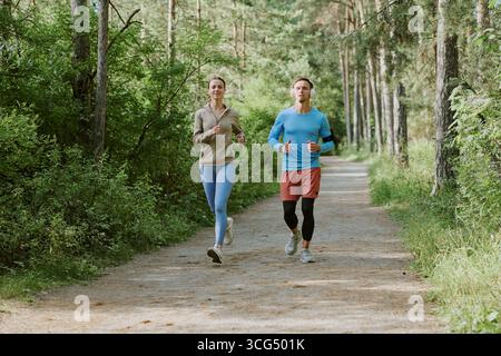 Kaukasische junge Erwachsene joggen gemeinsam auf dem Forest Trail in der Morgensonne Stockfoto