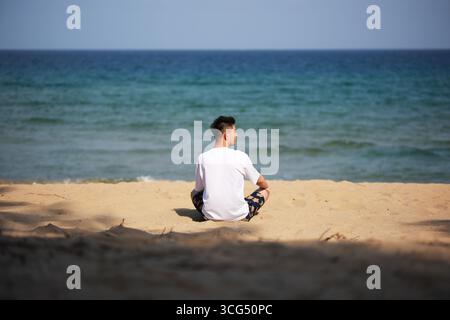 Der Mann sitzt am Sandstrand am Meer in Sanya, Hainan, China Stockfoto