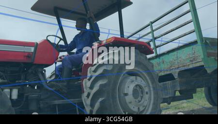 Fahrender Mann in blauen Overalls, der roten Traktor auf dem ländlichen Feld mit grünem Anhänger lenkt, Kopierraum Stockfoto
