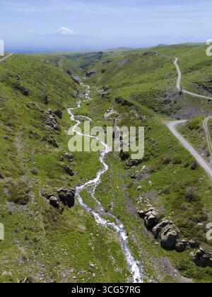 Ein Panoramablick zeigt einen Fluss, der durch eine grüne, hügelige Landschaft fließt, aus der Luft, Fluss und Schlucht Arkashian, im Hintergrund Mount Ararat in Tur Stockfoto