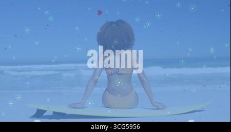 Sitzende Frau in gelbem Bikini, die auf den Sandstrand zum Meer blickt, mit gelbem Surfbrett Stockfoto